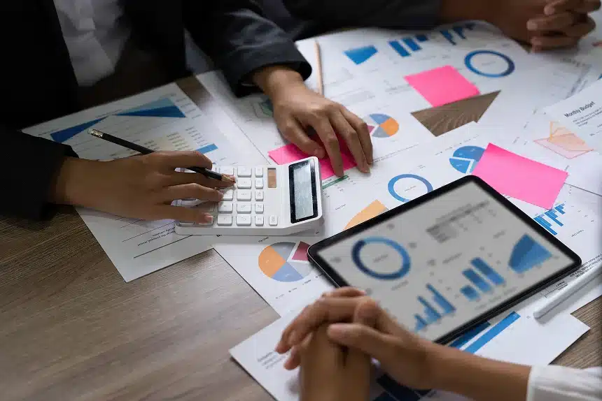 Business professionals collaborating at a table, surrounded by papers and calculators, focused on their work.