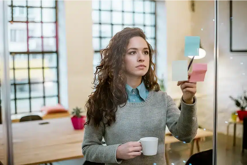 A woman holding a coffee cup, gazing thoughtfully at a sticky note on a table.