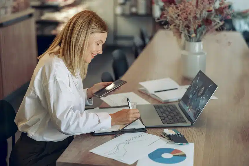 Woman focused on her laptop at a desk, surrounded by papers and a pen, engaged in work.
