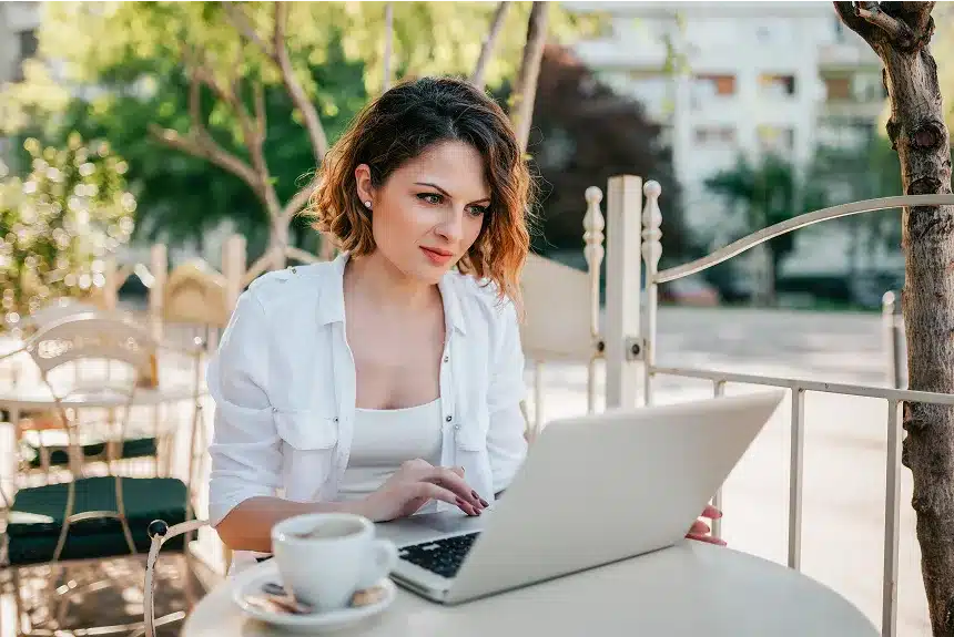 A woman sitting at a table, focused on her laptop, with a calm and organized workspace around her.