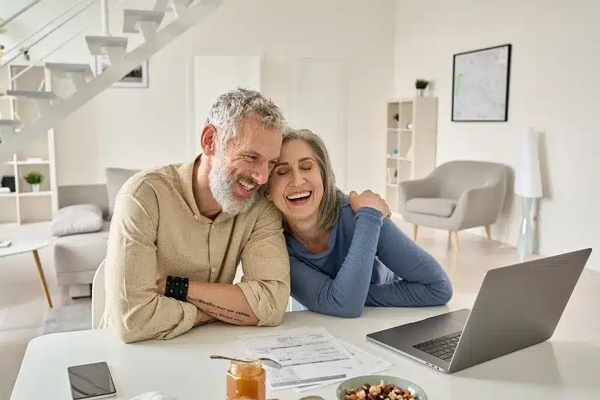 A smiling couple sitting at a table, engaged with a laptop in front of them, creating a warm and inviting atmosphere.