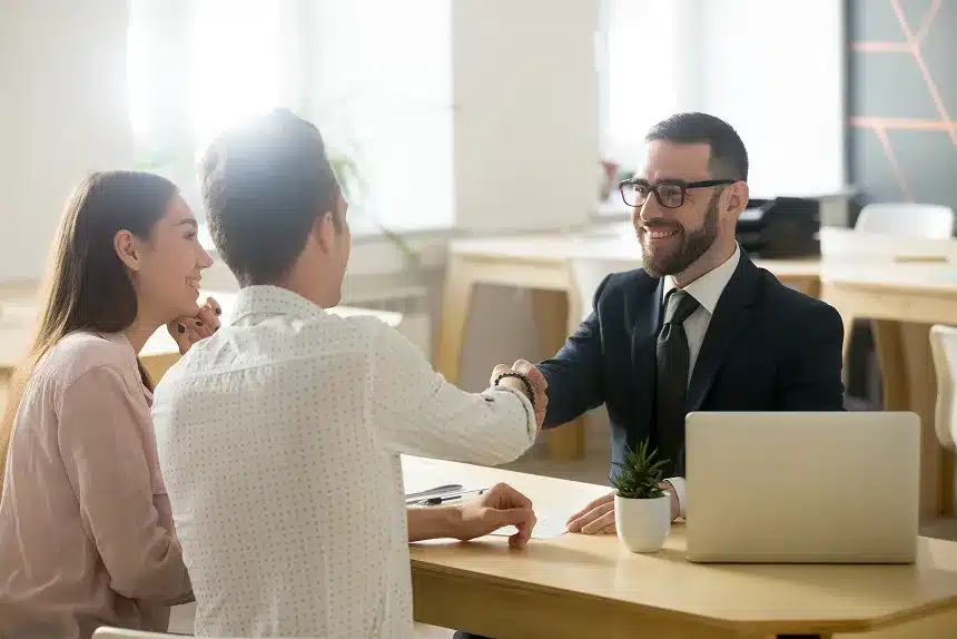 A man and woman shaking hands across a table, symbolizing agreement or partnership in a professional setting.