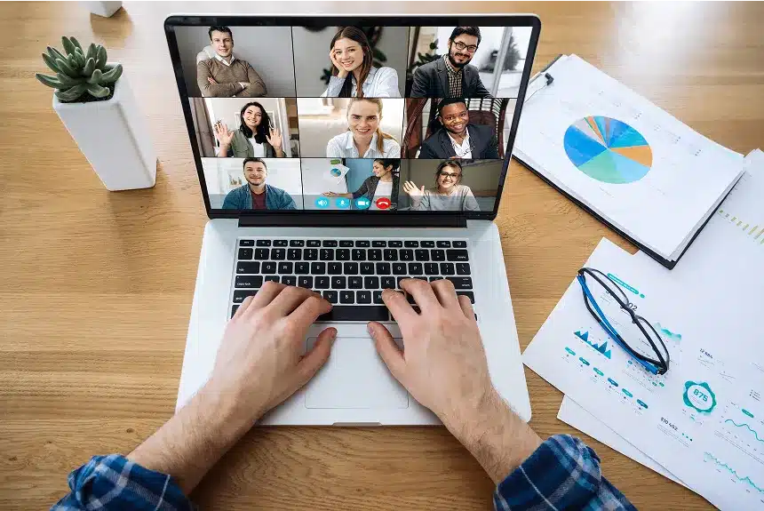 A person types on a laptop, with a group of people displayed on the screen, engaged in a virtual meeting.