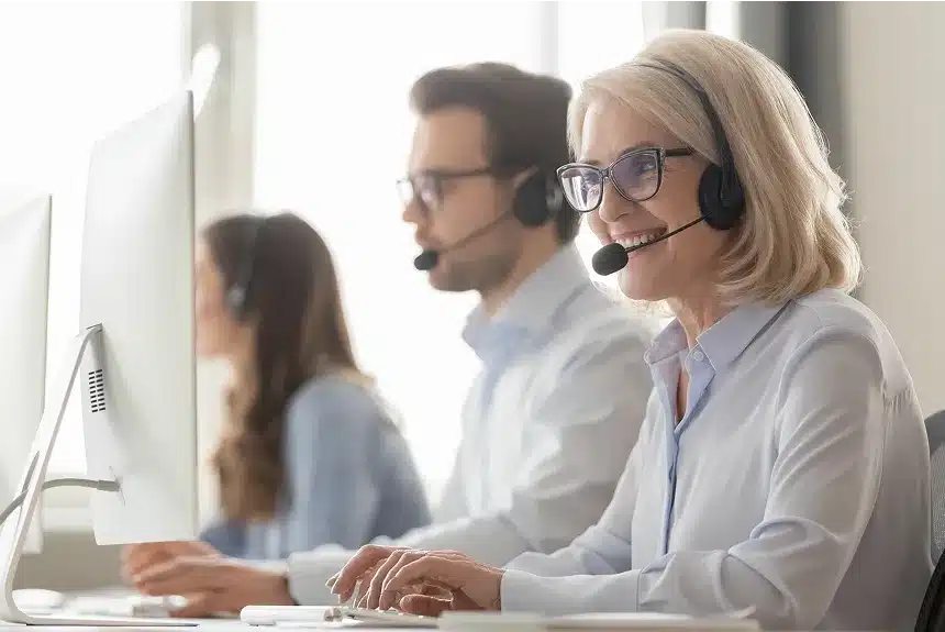 A woman with headphones and a headset is focused on her work at a computer.