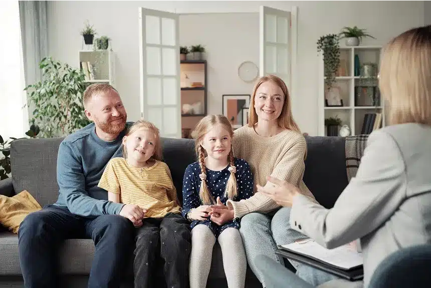 A family sits on a couch, with a child in a chair beside them, creating a cozy living room scene.