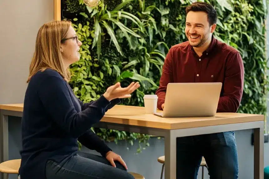 A man and woman sit at a table, collaborating on a laptop, engaged in discussion and sharing ideas.