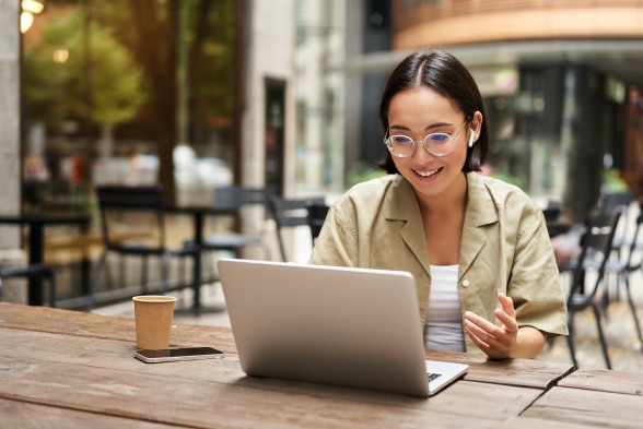 A woman wearing glasses is seated at a table, focused on her laptop while working or studying.