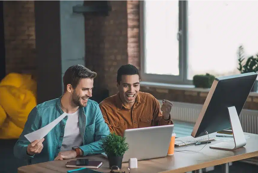 Two men seated at a desk, focused on a laptop, engaged in discussion or collaboration.