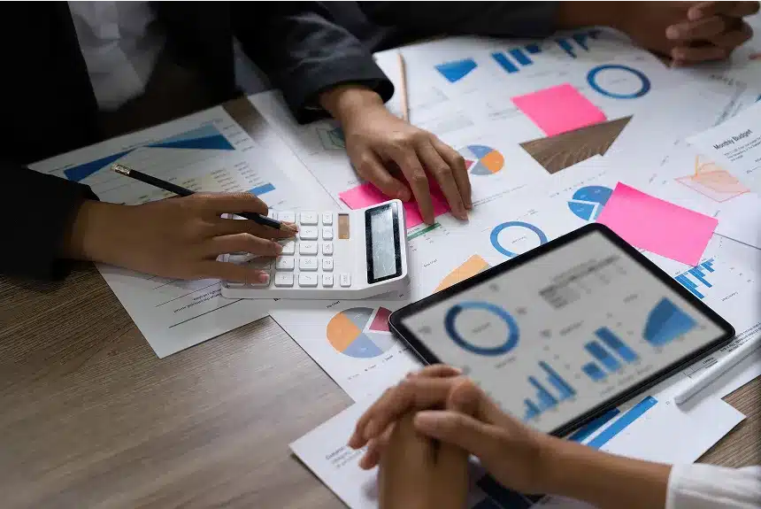 Business professionals collaborating at a table, surrounded by papers and calculators, focused on their work.