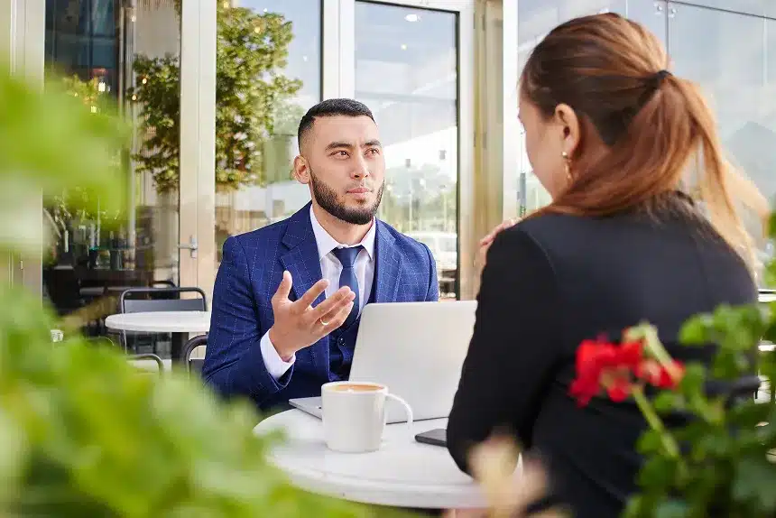 A man and woman sit at a table, working together on a laptop.