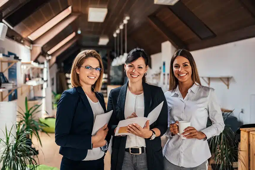 Three business women standing together in a modern office, engaged in conversation and collaboration.