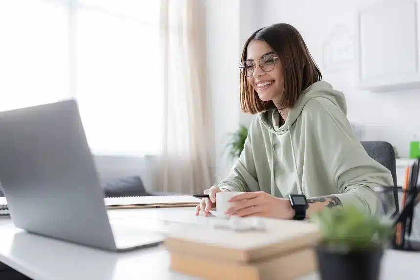 A woman wearing glasses sits at a desk, focused on her laptop while working.