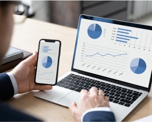 Businessman analyzing graphs on a laptop while simultaneously using a mobile phone for data insights.