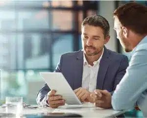 Two men in business suits examining a tablet, engaged in a discussion or analysis of the displayed information.