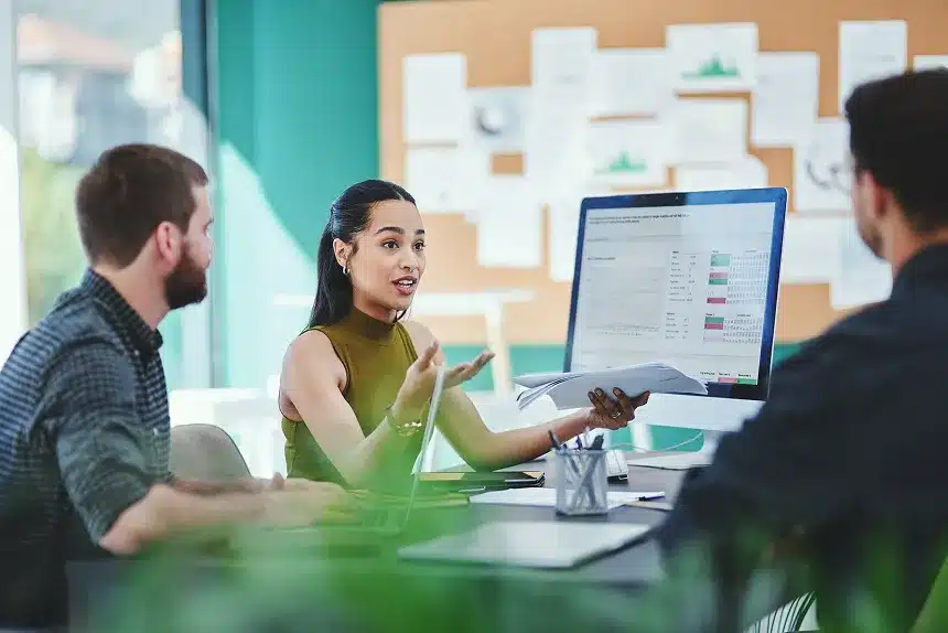 A woman engages in conversation with two men in a modern office setting, surrounded by desks and office equipment.