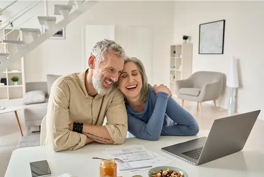A smiling couple sitting at a table, engaged with a laptop in front of them, creating a warm and inviting atmosphere.