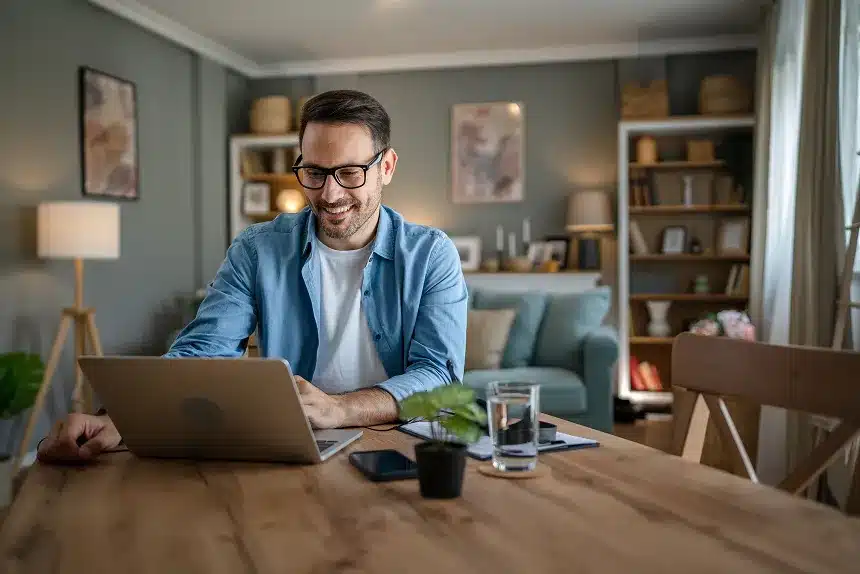 A man wearing glasses sits at a table, focused on his laptop while working or studying.