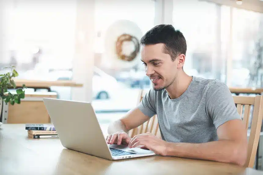 A man smiles while working on a laptop, conveying a sense of enjoyment and engagement with his task.