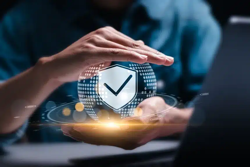 Man holding a laptop displaying a shield icon, symbolizing security and protection in technology.