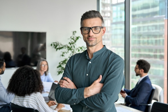 A man wearing glasses stands confidently before a group of attentive individuals, engaging them with his presence.