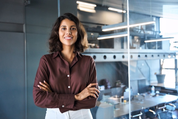 A professional woman in a business shirt stands confidently before a sleek glass wall, embodying a modern workplace environment.