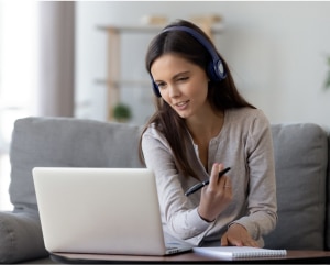 A woman wearing headphones is focused on her laptop, engaged in work or a virtual meeting.