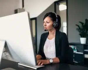 A woman wearing headphones, focused on her work at a computer, immersed in her task.