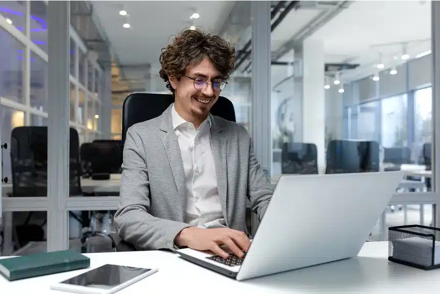 A man in a suit focused on his laptop, engaged in work at a modern office setting.