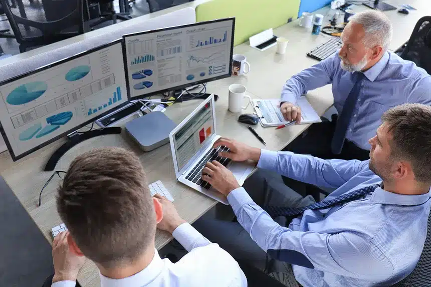Three men in business attire seated at a desk, collaborating over a laptop.
