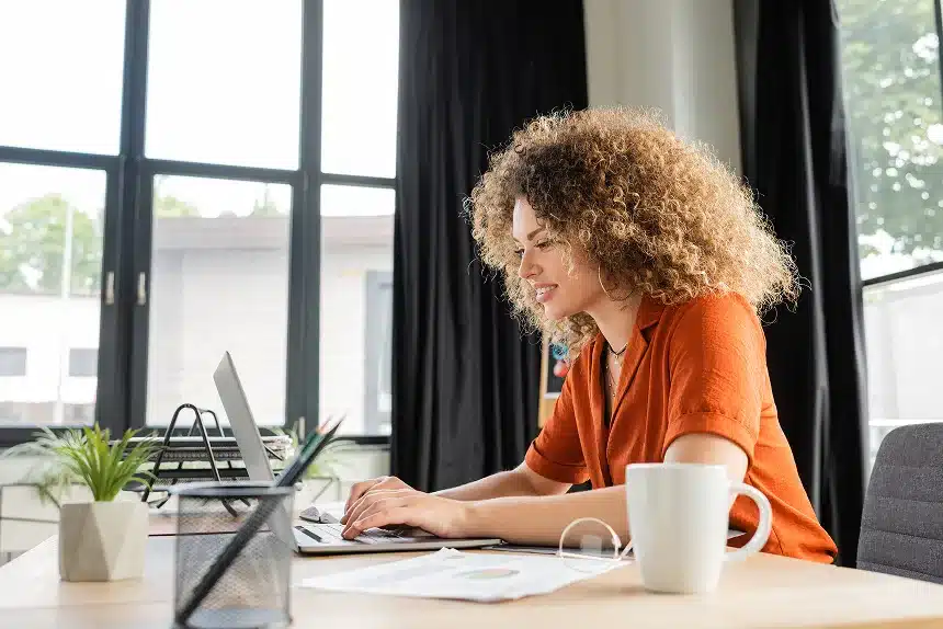 A woman with curly hair is seated at a desk, working on a laptop.