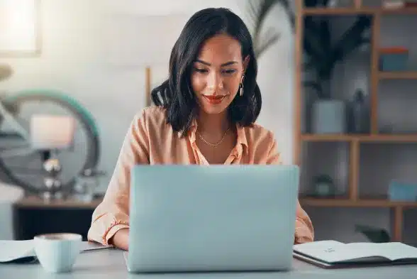 A woman seated at a table, focused on her laptop, engaged in work or study.