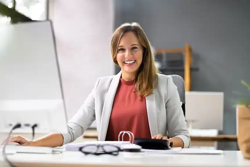 A woman smiling while seated at a desk, conveying a sense of happiness and contentment in her workspace.