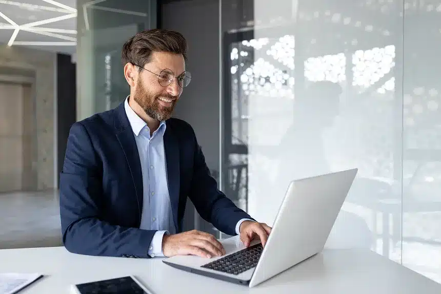 A man in a suit is focused on his laptop, working intently in a professional setting.