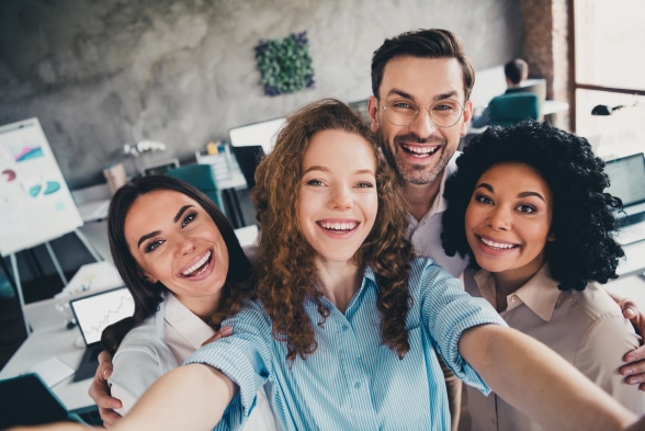 Four cheerful individuals pose for a selfie in a modern office setting, capturing a moment of camaraderie and joy.