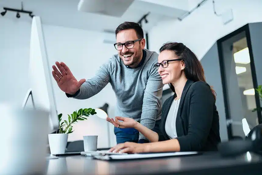 A man and woman smile together while viewing a computer screen, sharing a moment of joy and collaboration.