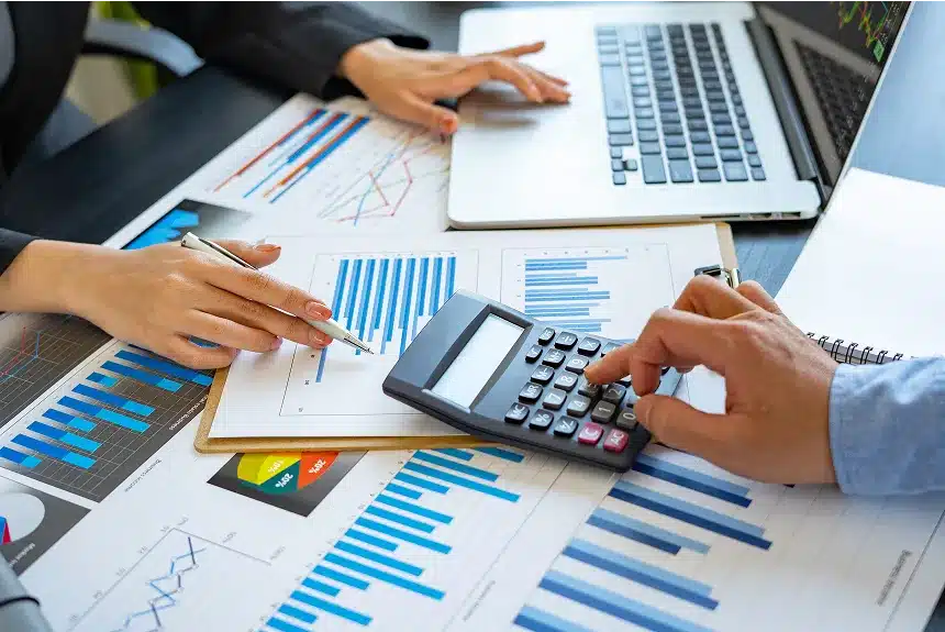 A group of business professionals collaborating on a laptop while using a calculator for calculations and data analysis.