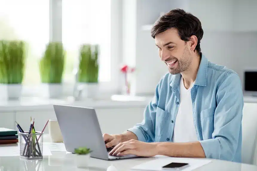 A man smiles while working on his laptop, conveying a sense of enjoyment and engagement with his task.