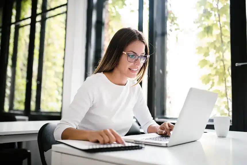 A woman wearing glasses is focused on her laptop, engaged in work at a desk.