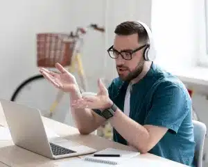 A man with headphones and glasses is seated at a desk, focused on his laptop.