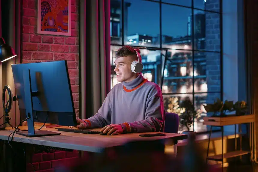 A man with headphones sits at a desk, focused on a computer screen in a well-lit workspace.