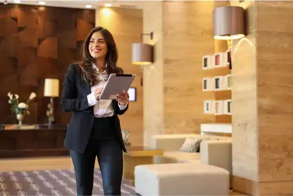 A professional woman in a business suit confidently holds a tablet, showcasing her engagement in a work-related task.