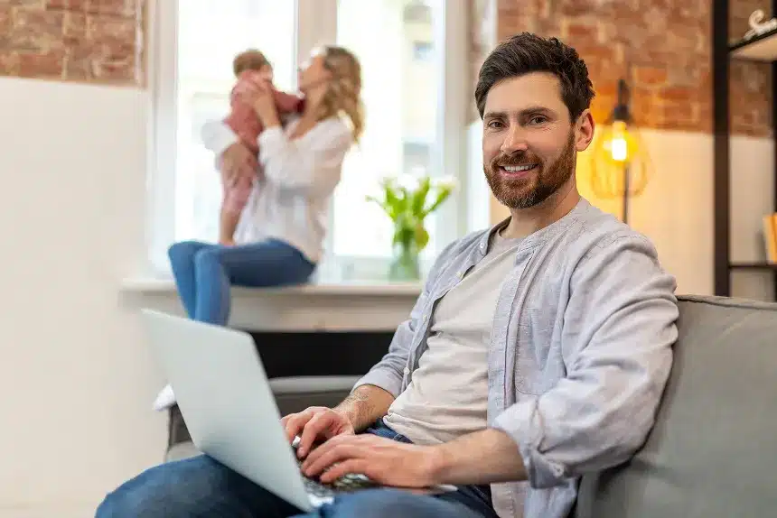 A man sitting on a couch, focused on his laptop, with a relaxed posture and a cozy living room setting.