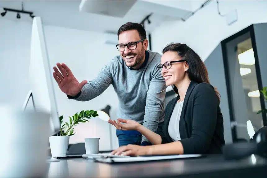 A man and woman smile together while viewing a computer screen, sharing a moment of joy and collaboration.