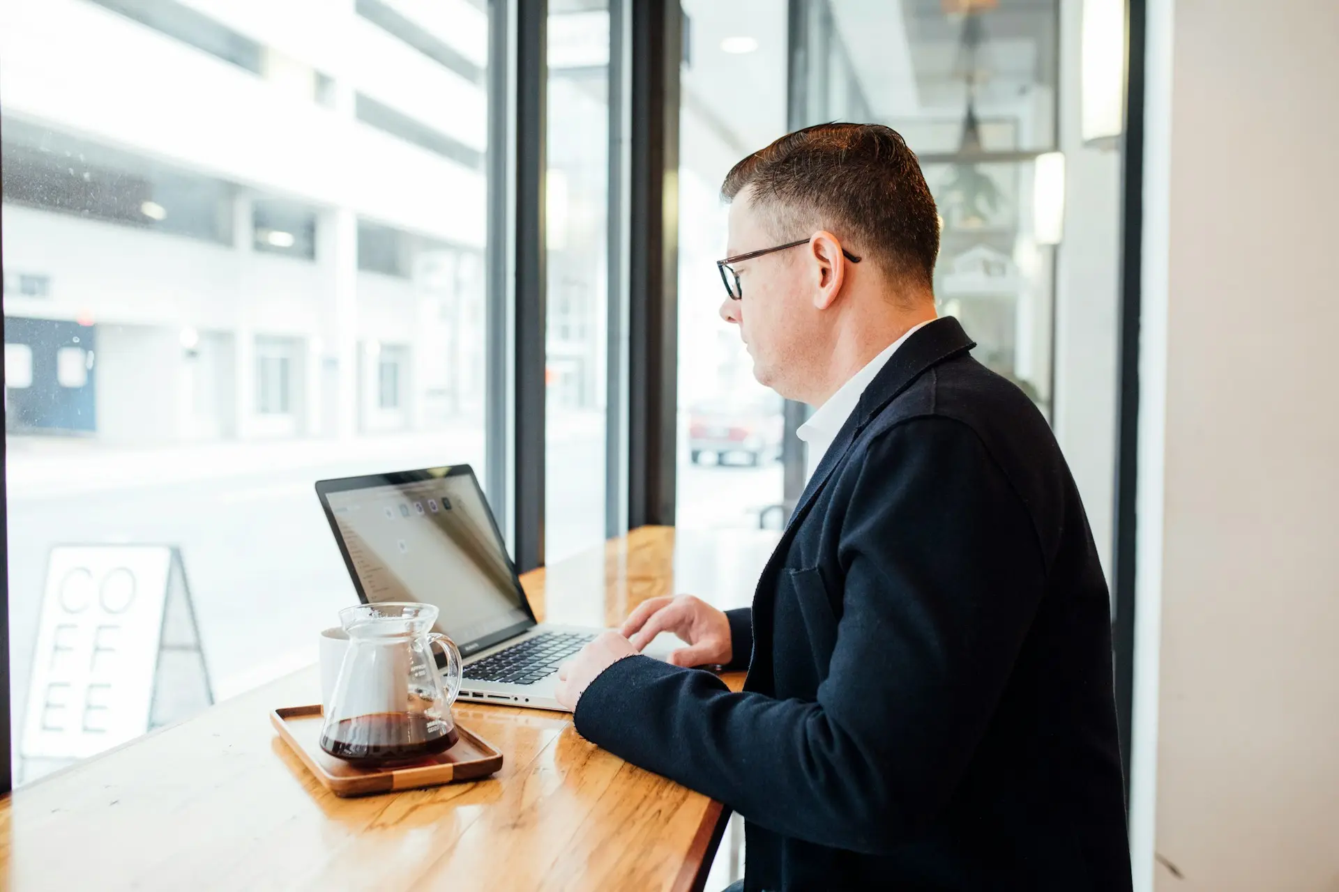 A man in a suit sits at a table, focused on his laptop, with a professional demeanor.