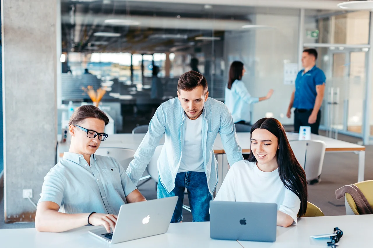 Three individuals focused on their laptops while collaborating in a modern office environment.