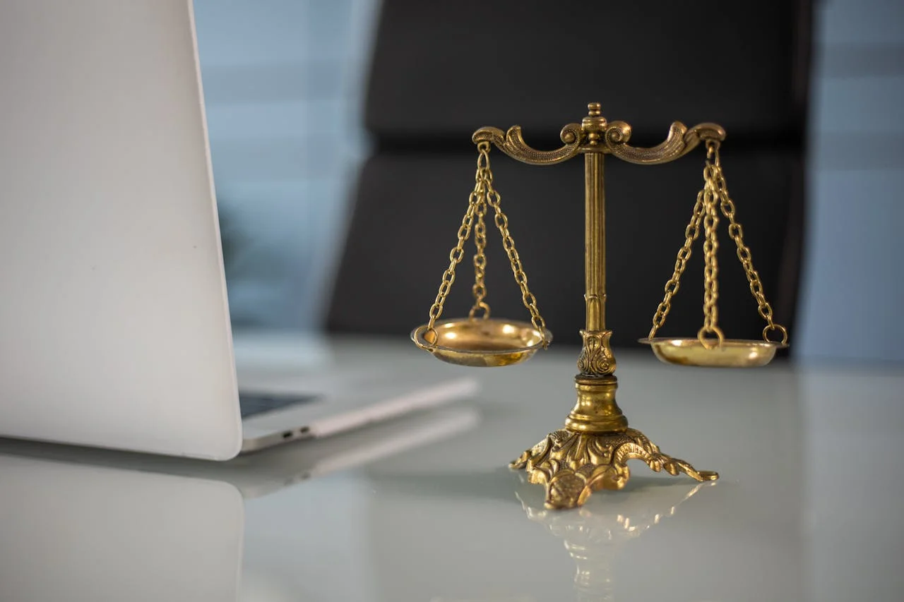 Golden scales of justice on a desk beside a laptop, symbolizing law and fairness in a professional setting.