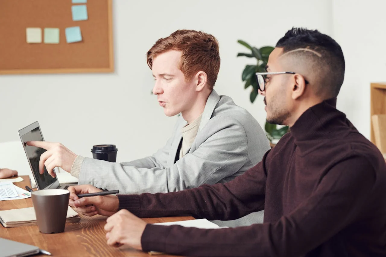 Three men seated at a table, each using a laptop, engaged in discussion or collaboration.