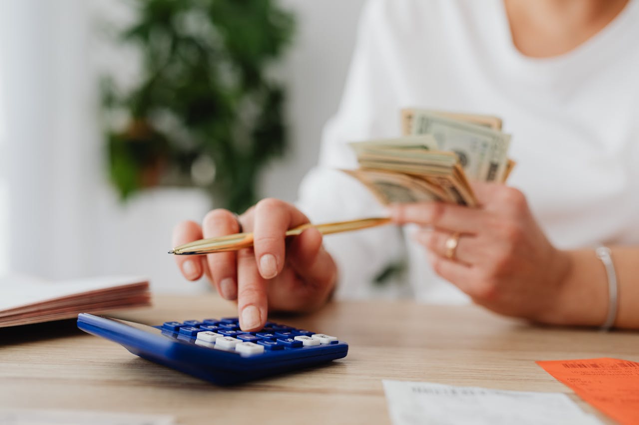 A woman counts cash while using a calculator, focused on her financial calculations.