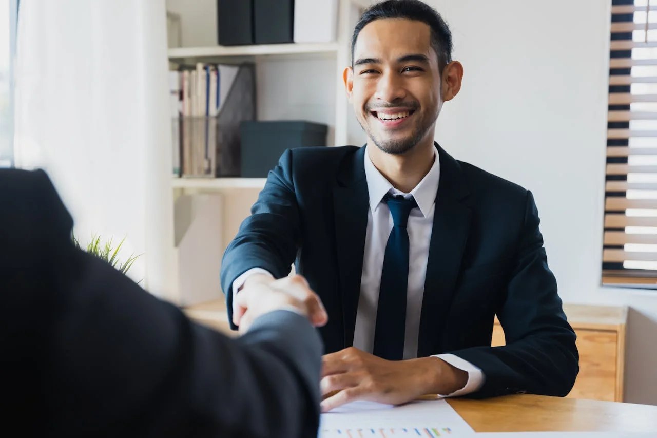 A man in a suit shakes hands with another man, symbolizing a professional agreement or greeting.
