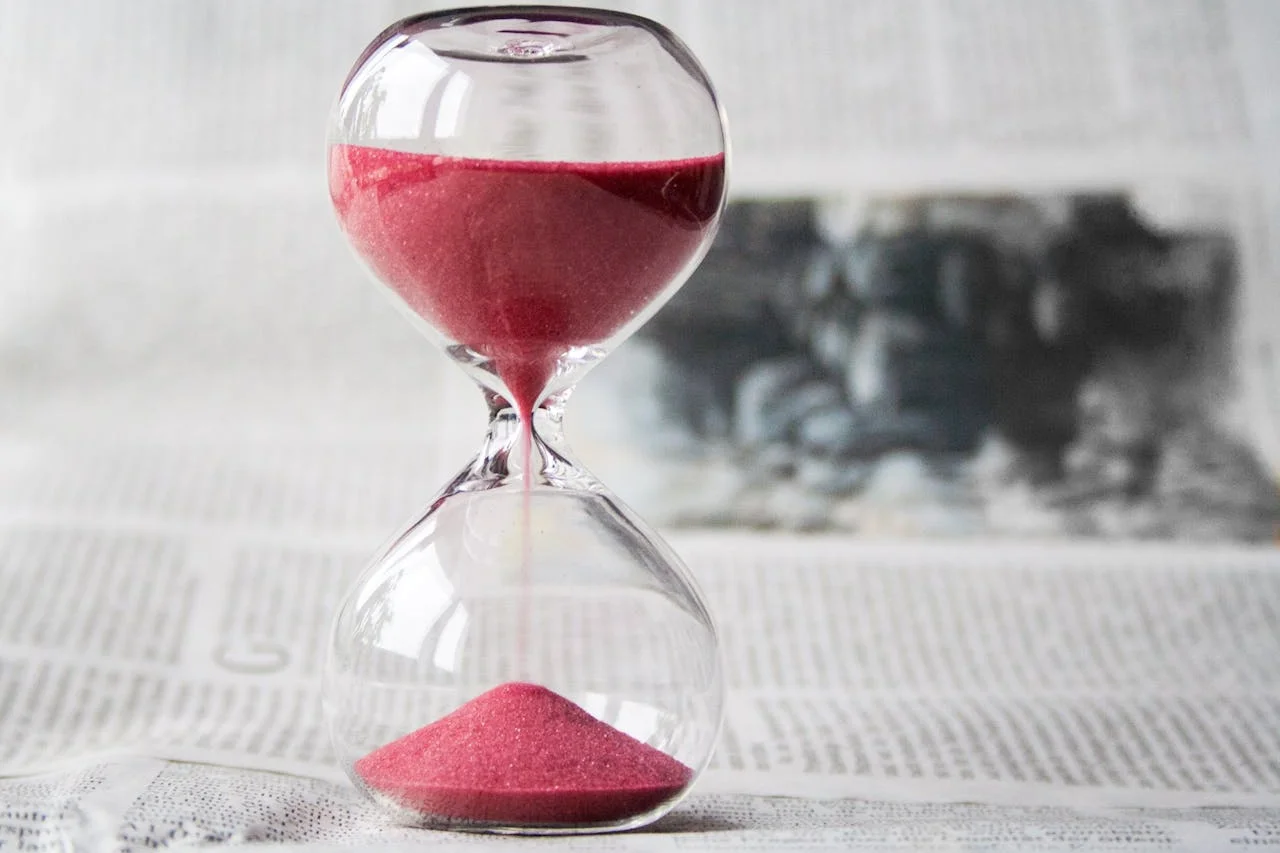 An hourglass filled with pink sand rests on top of a newspaper, symbolizing the passage of time and current events.